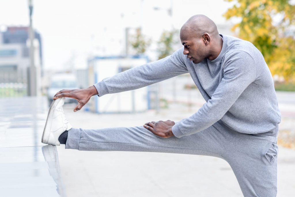 Black man doing stretching before running in urban background to illustrate The Role of Exercise and Physical Activity in Weight Loss